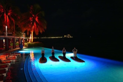 水中ライトが幻想的に輝く夜のプールで、静かにヨガを楽しむ人々。