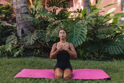 ピンクの建物を背に、静かに目を閉じて深呼吸する女性。穏やかな癒しの時間。