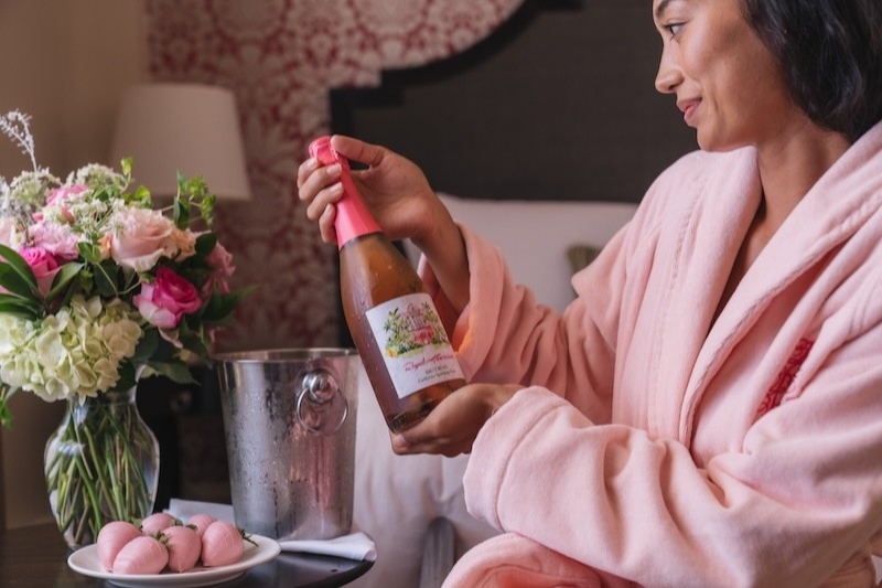 ロイヤル ハワイアンの客室で、ピンクのバスローブを着た女性がロイヤル ハワイアン限定スパークリングワインを手にしている様子