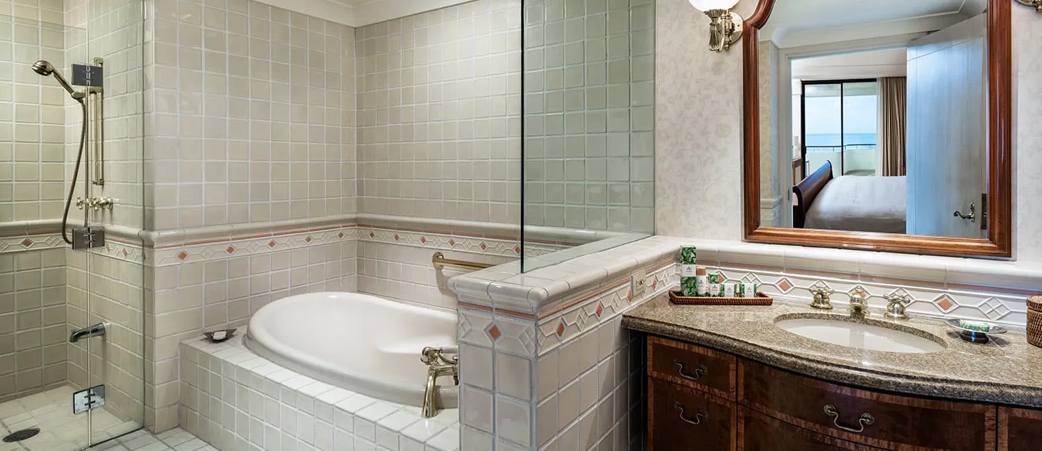 浴槽と洗面台を備えたアリイスイートのバスルーム。鏡越しにベッドルームと海が見える