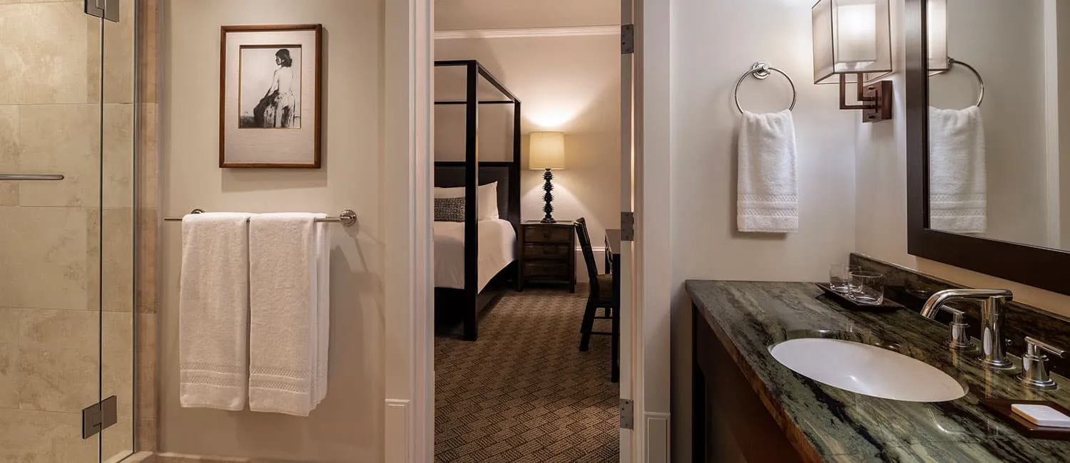 洗面台とシャワーを備え、奥にベッドルームが見えるクイーンカアフマヌスイートのバスルーム