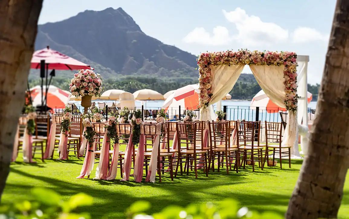 ダイヤモンドヘッドを背景に、ピンクのリボンで装飾されたチェアが並ぶガーデンウェディングの挙式会場