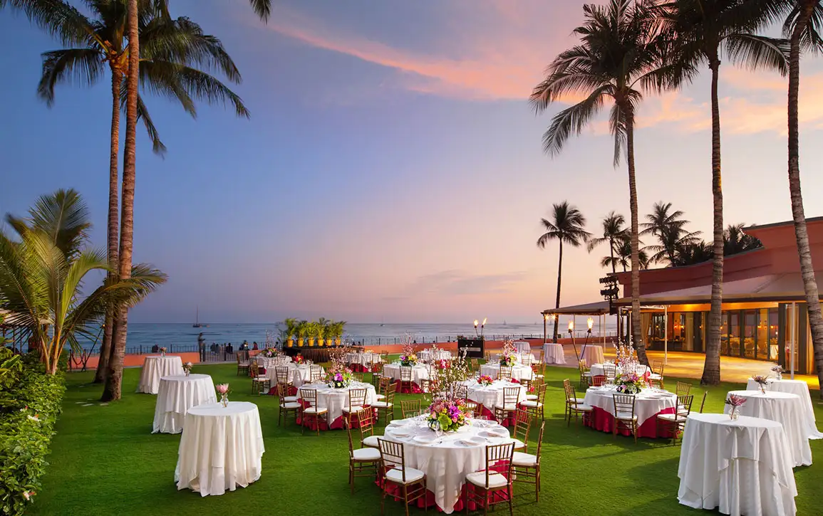 夕暮れの空と海を背景に、装花で彩られた円卓が並ぶオーシャンフロントのナイトウェディング会場