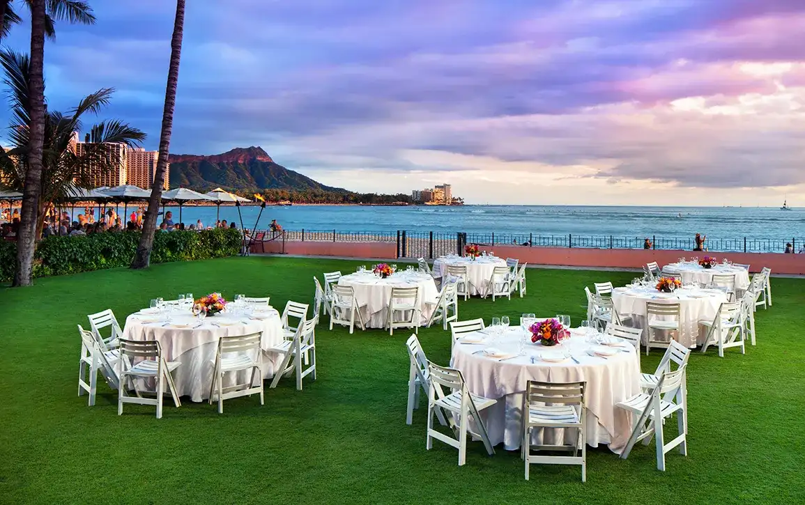 ダイヤモンドヘッドとワイキキの海を望む芝生に、白いクロスをかけた円卓が並ぶ屋外ウェディングレセプション会場
